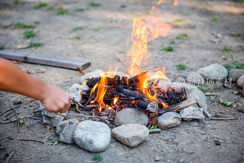 Burning forest at night. Campfire in a tourist camp outdoors in the mountains. Flame and fire sparks on a dark abstract background. We are preparing an outdoor barbecue. Infernal element of fire. Fuel, power and energy. Bonfire by the water in the forest
